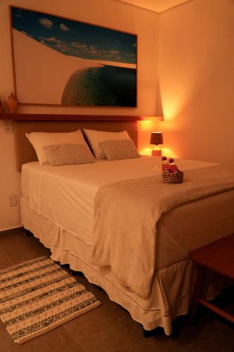 a bedroom with a white bed with a painting on the wall at Pousada Vila Pequi in Barreirinhas