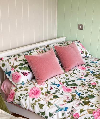 a bed with pink pillows and a floral quilt at Whitethorn Shepherds Hut in Bellaghy