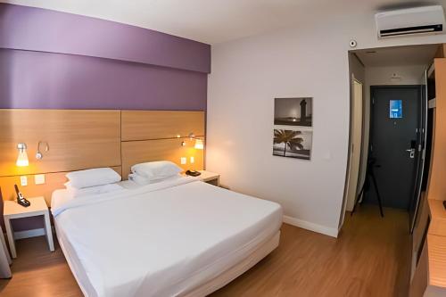 a bedroom with a large white bed and a purple wall at Stay Inn Santos in Santos