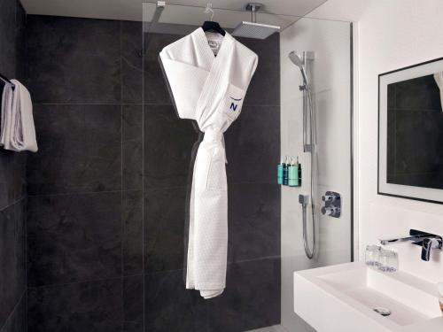 a bathroom with a shower and a white robe hanging on a wall at Novotel Kinshasa La Gombe in Kinshasa