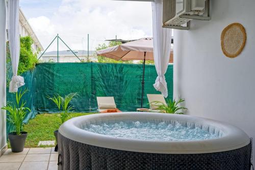 a bath tub in a yard with an umbrella at Nid rose paradis secret au robert avec jacuzzi in Le Robert