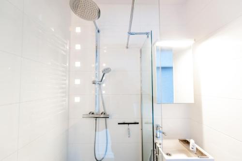 La salle de bains blanche est pourvue d'une douche et d'un lavabo. dans l'établissement Bluebeach Scheveningen, à Scheveningen
