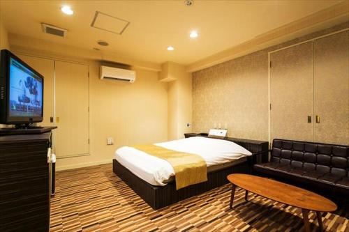 a bedroom with a bed and a couch and a television at Hotel WILL Kashiwa in Kashiwa