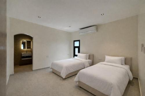 two beds in a room with white walls at Etlaala Chalet in Ibri