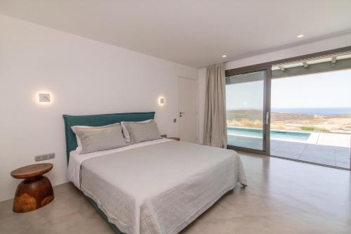a white bedroom with a bed and a large window at Tinos Prinos 3 in Agios Fokas