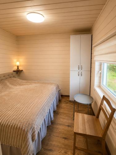 a bedroom with a bed and a chair and a window at Atpūtas mājas Leiksnīte in Vaikulāni