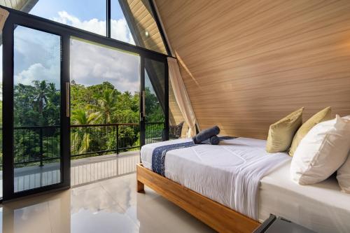 a bedroom with a bed and large windows at Green Tara Valley Ubud by Betterplace in Ubud