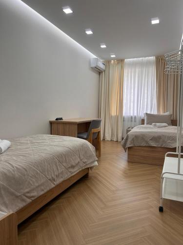 a bedroom with two beds and a desk and a window at Modern Apt in Shymkent