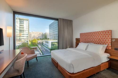 a bedroom with a bed and a desk and a large window at Windmill Frankfurt Niederrad in Frankfurt