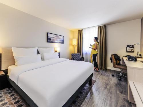 a woman standing in a hotel room with a large bed at Mercure Hotel München Süd Messe in Munich