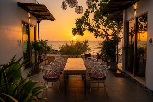 a long table with chairs and the ocean at sunset at Ma's Sea Beach House in Klong Muang Beach