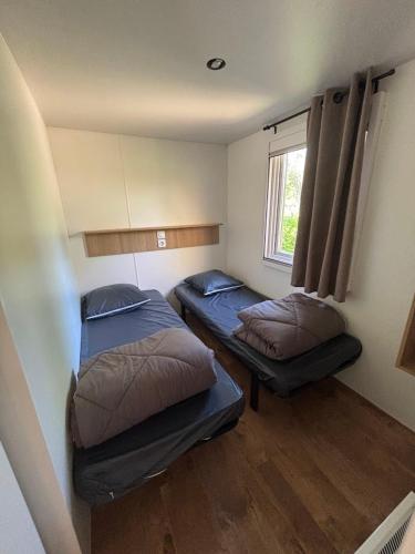 two beds in a small room with a window at Flower Camping Les Mijeannes in Rieux-de-Pelleport