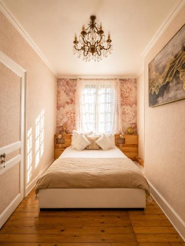 a bedroom with a bed with a chandelier and a window at La Cour Du Puits, Chambre Darjeeling in Cormeilles