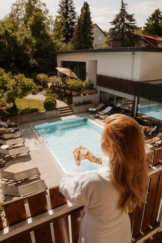 Eine Frau steht auf einem Balkon in der Nähe eines Schwimmbeckens. in der Unterkunft Vulkanlandhotel Legenstein in Bad Gleichenberg