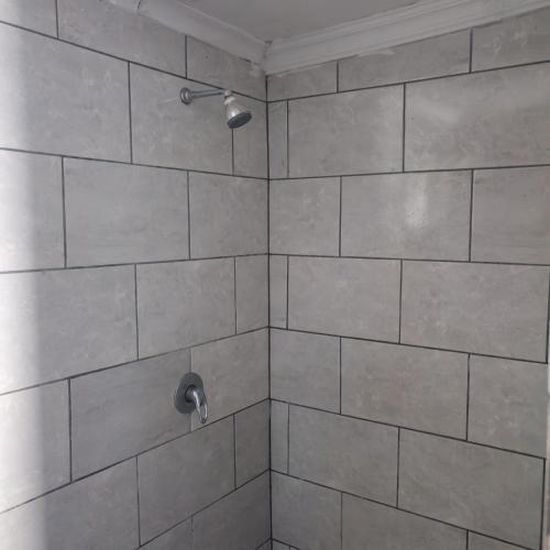a bathroom with a shower with a tile wall at Prime Guest Inn in Benoni