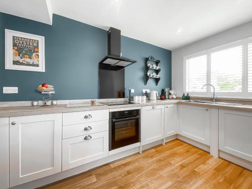 a kitchen with white cabinets and a blue wall at Taigh Beag in Stranraer