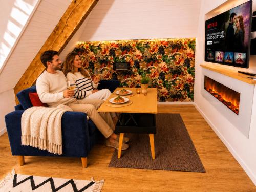 a man and woman sitting on a couch in a living room at MRODBNB - Appart Neuf - Vue Mer - 25m Plage & Resto - Ciné - cheminée - Popcorn in Cancale