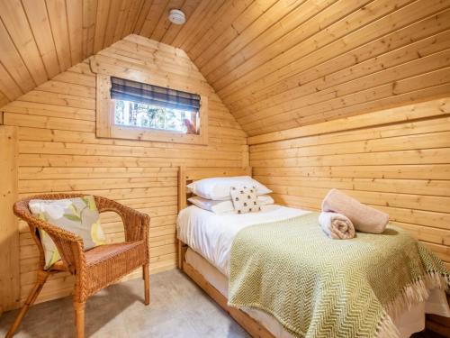 a bedroom with a bed and a chair in a log cabin at Chalet Forester's Bothy by Interhome in Coldstone