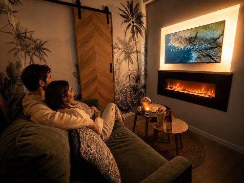 a man and woman sitting on a couch in front of a fireplace at MRODBNB - Appart Neuf - Aperçu Mer - 25m Plage & Resto - Ciné - Cheminée - Popcorn in Cancale