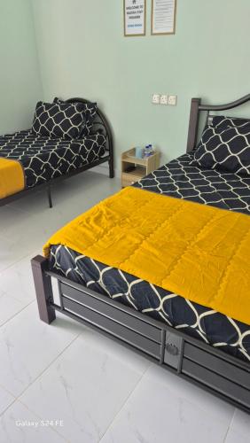 two beds in a room with yellow and black sheets at ZIRA STAY PENARIK - Ziyad Room in Kampong Ru Sepuloh