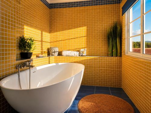 a yellow tiled bathroom with a tub and a window at Quinta do Sol Ocean Villa with Spa Bath & Volcano Views in Rabo de Peixe