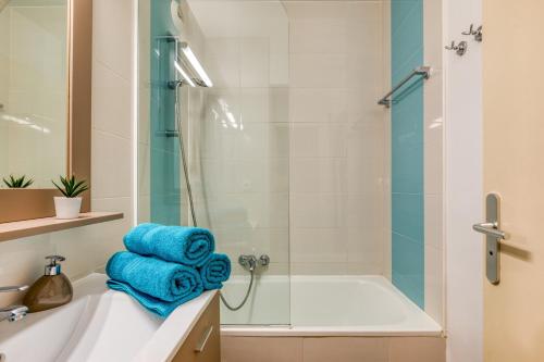a bathroom with a shower and a bath tub with blue towels at Le Murmure des palmiers in La Grande Motte
