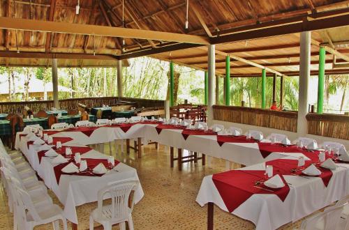 um quarto com mesas brancas e cadeiras com guardanapos vermelhos em Hosteria El Paraiso de las Orquideas em Archidona