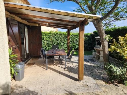 a wooden pergola with a table and chairs on a patio at Maison à la mer in Vendres