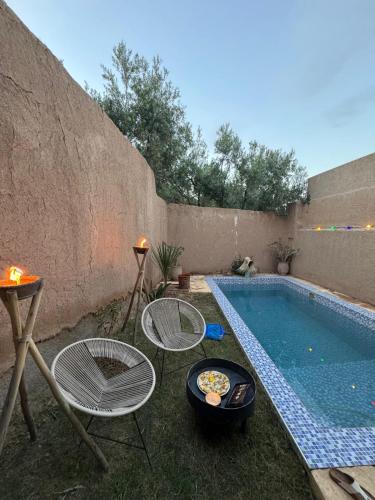 a swimming pool with two chairs and a table with a tray of food at Gîte berbère in Tagadirt Alkadi