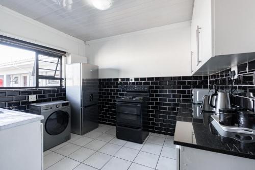 a kitchen with a washer and dryer and black tiles at Safi Elegant Self-catering Suite 5 in East London