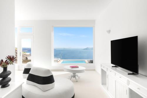 a white living room with a large window and a tv at Neraé Santorini in Imerovigli