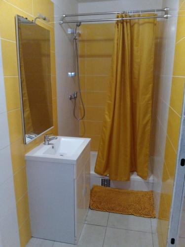a bathroom with a sink and a shower with a yellow shower curtain at Le petit coin de campagne in Le Robert