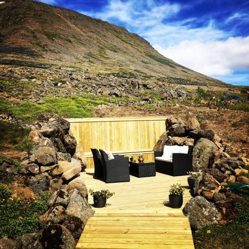 a wooden deck with black chairs and a hill at Guesthouse Stekkaból in Patreksfjörður
