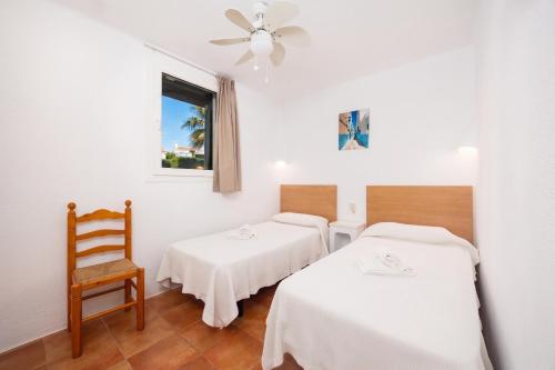two beds in a room with a chair and a window at Villa Binipaco in Binibeca