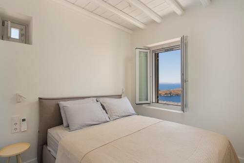 a white bedroom with a bed and a window at Serene Shore Serifos in Alona