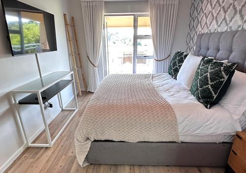 a bedroom with a bed and a desk and a window at The Fairway Apartment in Plettenberg Bay