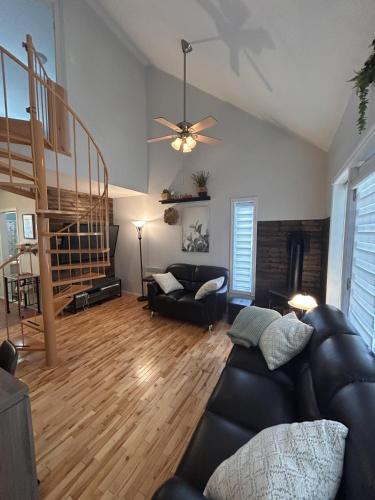 a living room with a black leather couch and stairs at La Cachette in LʼAnse-Saint-Jean