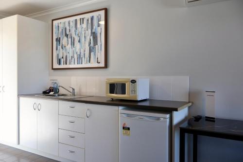 a kitchen with white cabinets and a microwave on a counter at Victory Hotel Motel Gympie in Gympie