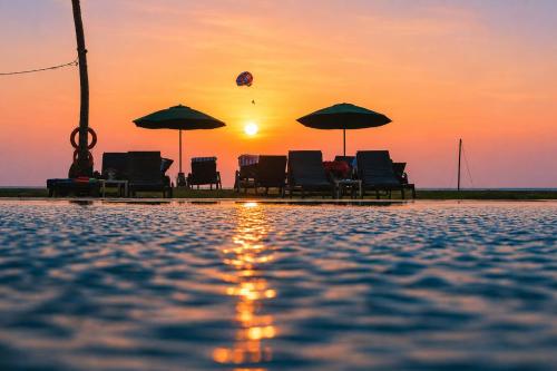 a group of chairs and umbrellas on the beach at sunset at Frangipani Langkawi Resort in Pantai Cenang