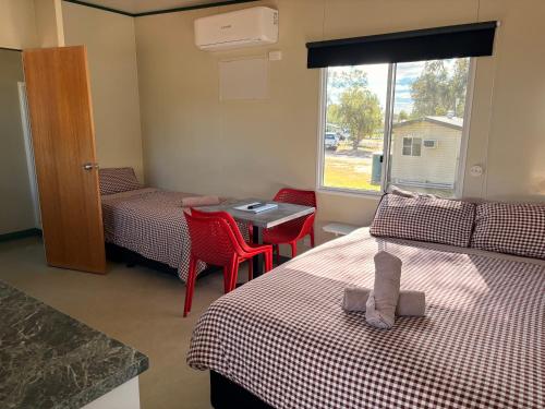 a room with two beds and a table and a window at Cunnamulla Tourist Park in Cunnamulla