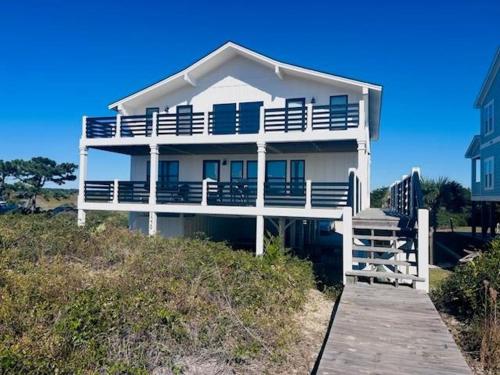 a white house on the beach with a wooden dock at Somewhere South home in Holden Beach