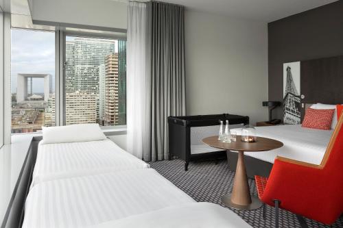 a hotel room with two beds and a table and a window at Meliá Paris La Défense in Courbevoie
