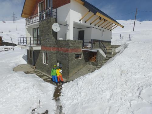 two people standing in the snow in front of a building at Mountain Cricket Chalets and Apartments Gudauri in Gudauri