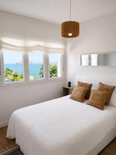a white bedroom with a white bed and two windows at Casa Roca Blanca Suances in Suances