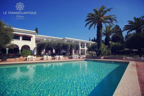 a swimming pool in front of a building with palm trees at Hotel Transatlantique in Mekn&egrave;s