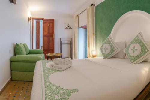 a bedroom with a white bed and a green chair at Hotel Larayhana in Fez