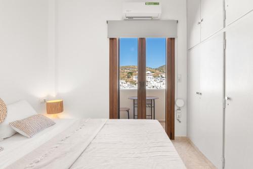 a white bedroom with a bed and a view of a city at Vivlos Stays - Ageri in Vívlos