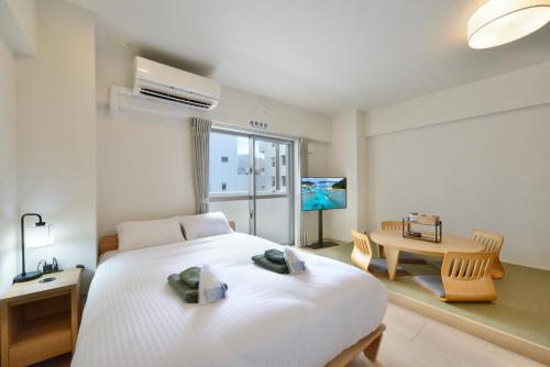 a bedroom with a large white bed and a table at Hotel HIRAKU RYUKYU -STYLE- in Naha