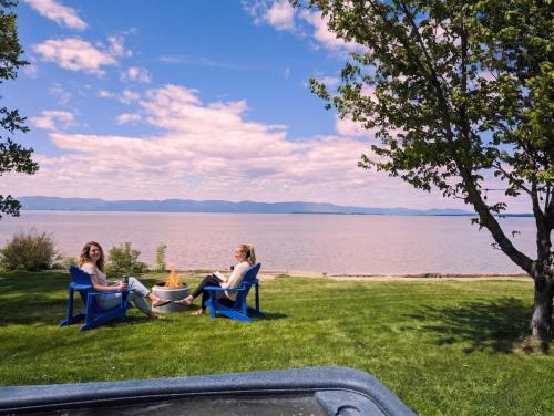 two women sitting in chairs on the grass by the water at Chalet #2 Waterfront with Spa, Fireplace Wifi & AC in Cap-Saint-Ignace