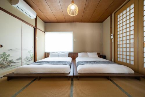 two beds in a room with a window at 湯のん - Yunon - 温泉付き一棟貸し古民家 指宿名物 砂むし温泉徒歩2分 最大11名 in Ibusuki